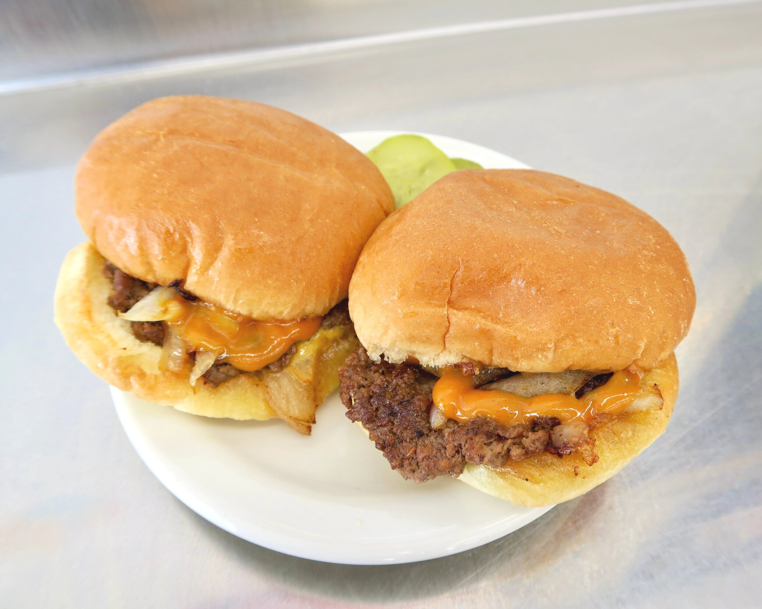 Two Bates' cheeseburgers on a plate with pickles
